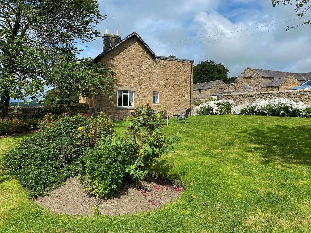 una casa con un patio verde con un arbusto en Paddock Cottage, en Alnwick
