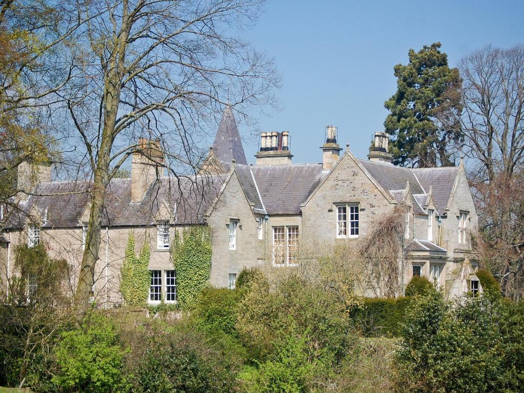 a large stone house in the middle of trees at Lochside Garden House - S4484 in Town Yetholm