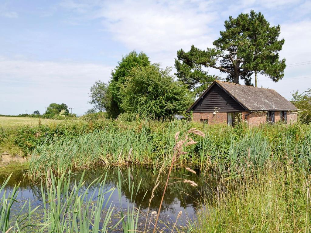 an old house in a field next to a pond at Stable Cottage in Ticehurst