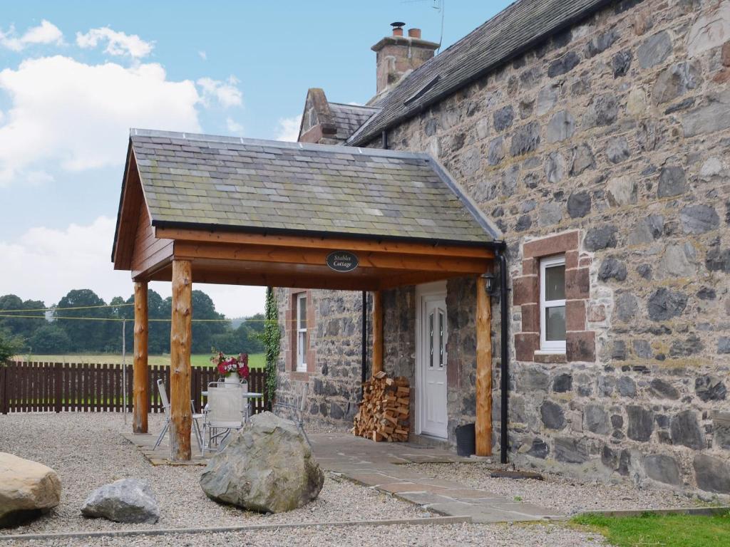 a stone building with a wooden pavilion in front of it at Stable Cottage - Beaufort Estate in Belladrum