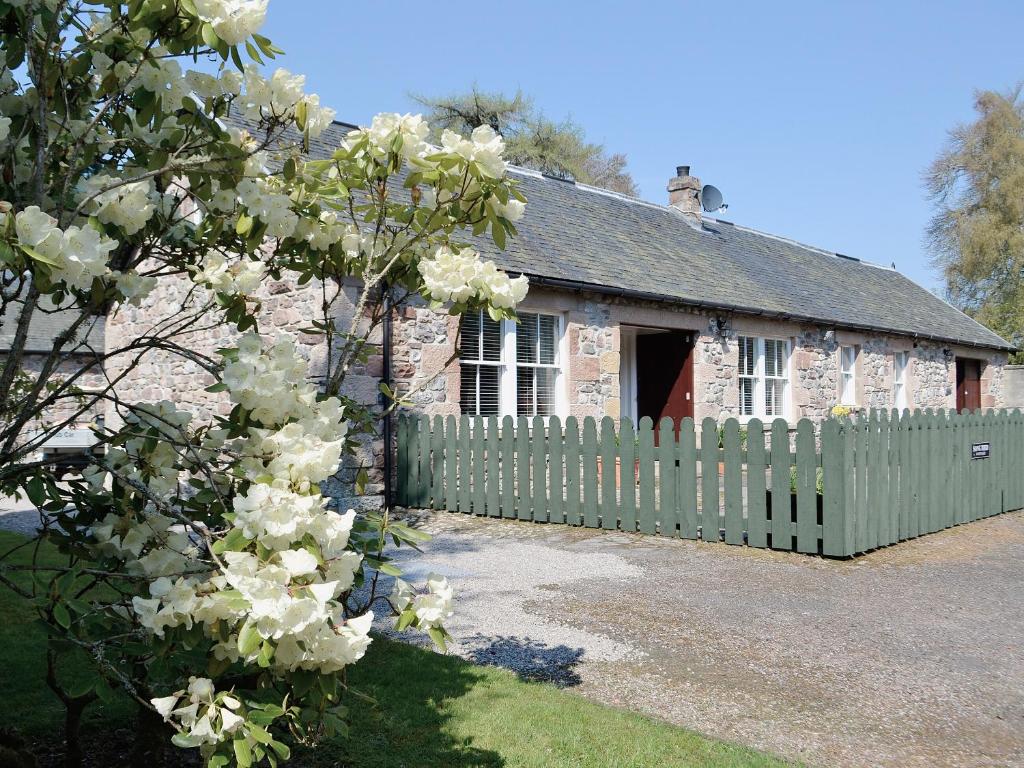 an old stone house with a fence and a flowering tree at Song Bird Cottage in Lochend