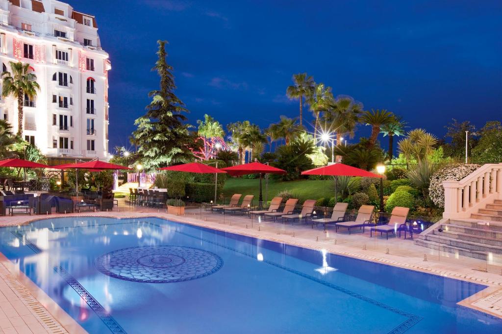 a swimming pool with chairs and red umbrellas at night at Hôtel Barrière Le Majestic Cannes in Cannes