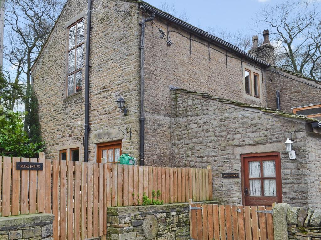 uma casa de tijolos com uma cerca de madeira em frente em Marl Farm Cottage em Hayfield