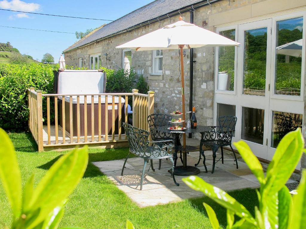un patio con mesa, sillas y sombrilla en Mill Cottage en Ravensworth