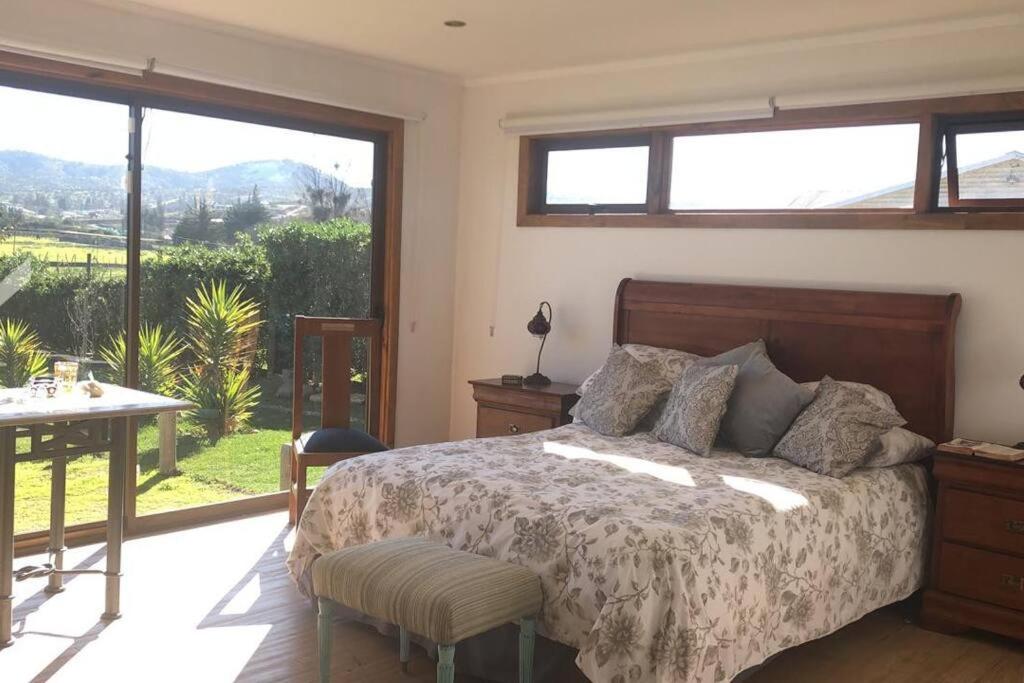 1 dormitorio con cama, mesa y ventanas en Hermosa y comoda casa de campo con vista al valle, en Limache