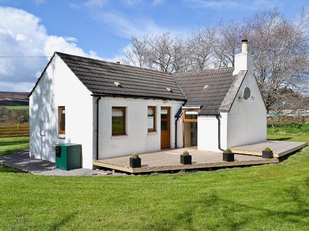 a small white house with a wooden deck at Shenval Cottage - 28280 in Glenlivet