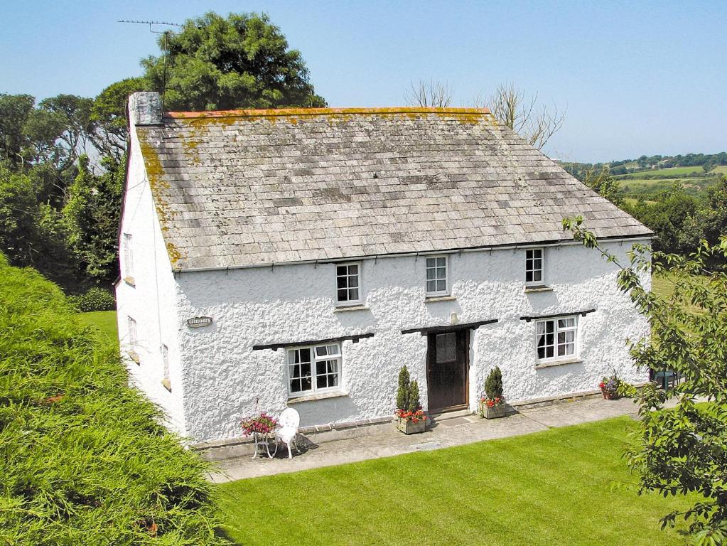 a white cottage on a hill with green grass at Gingers Cottage in Marhamchurch