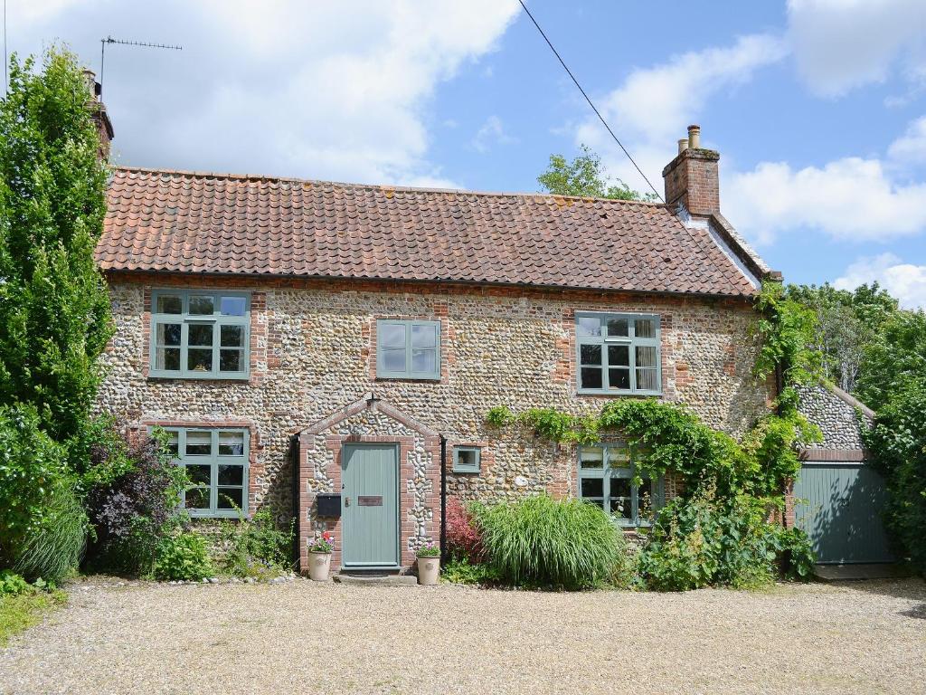 Chapel Cottage في Sharrington: كوخ من الطوب القديم مع باب أخضر