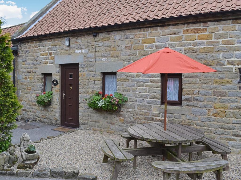 a wooden table with a red umbrella and two benches at Dairy Cottage - 28344 in Staintondale