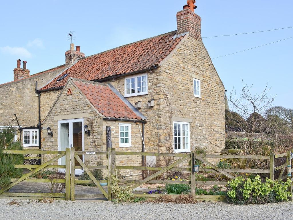 an old stone house with a wooden fence at Dragon Fly Cottage in Brompton