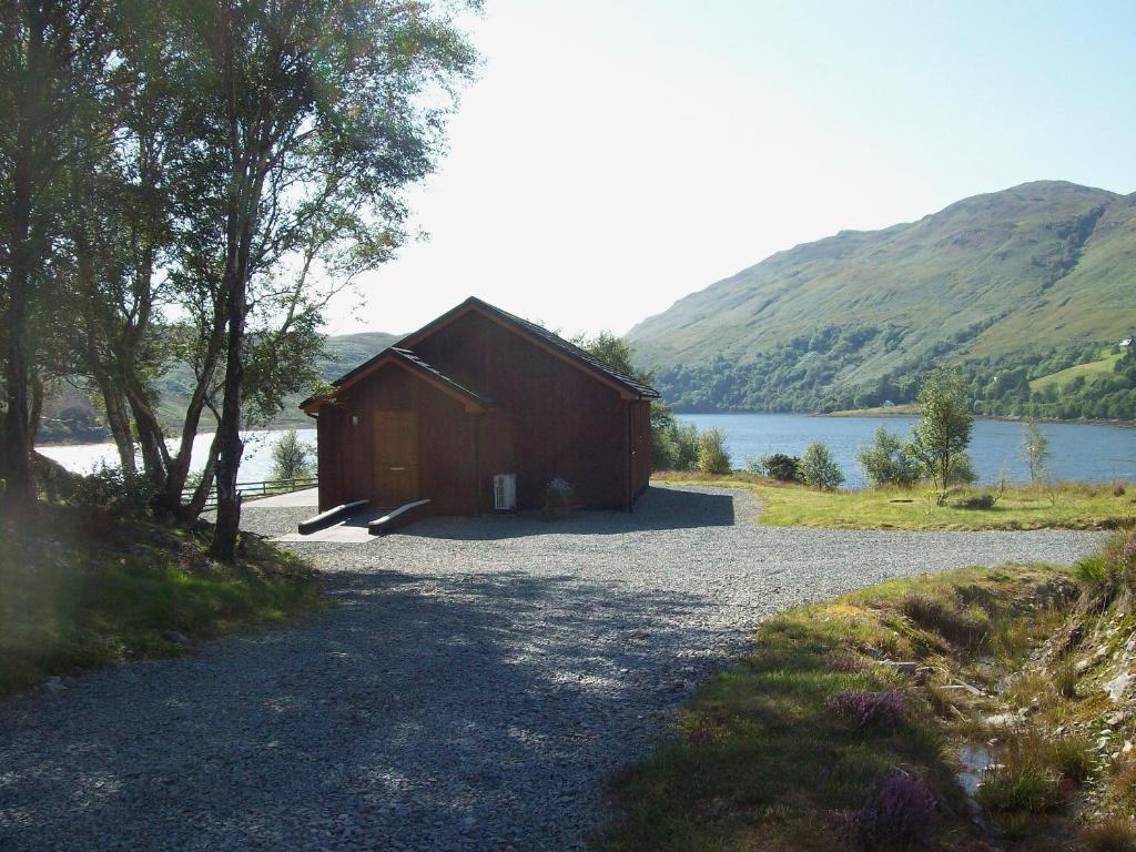 a small building on a gravel road next to a lake at Island Bay View in Sallachy