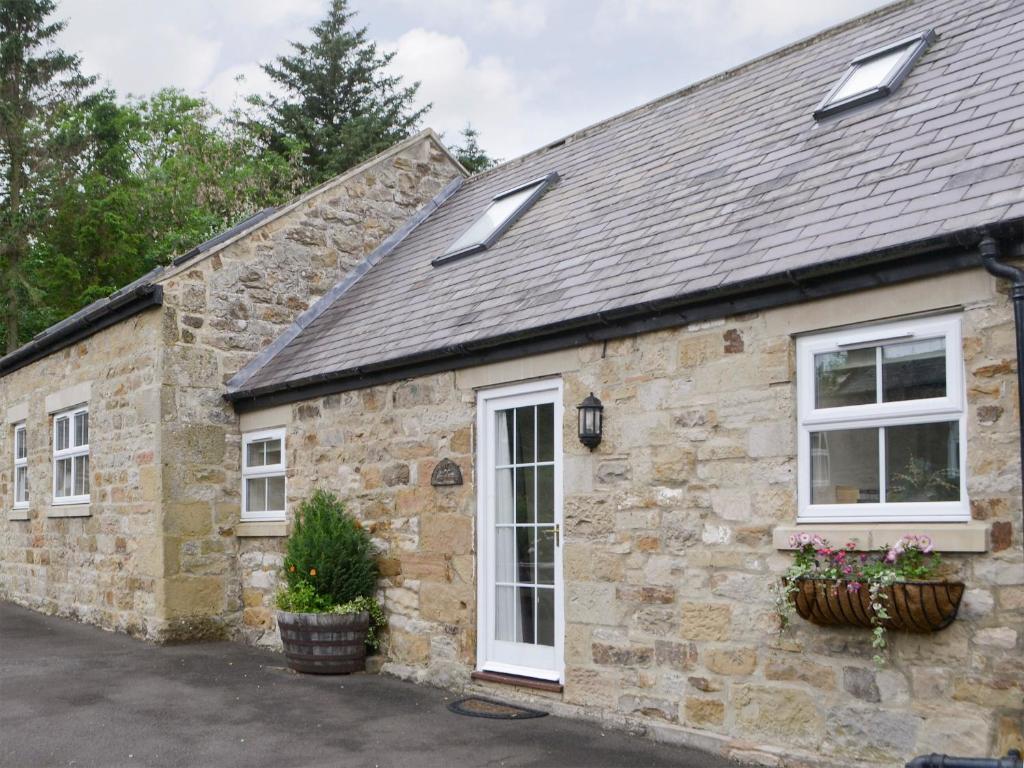 a stone house with white windows and plants at Piglet Cottage in Elsdon