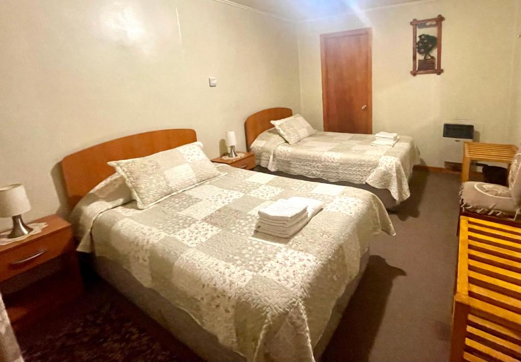Habitación de hotel con 2 camas con sábanas blancas en Hospedaje Baquedano, en Puerto Natales