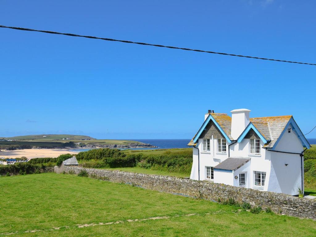 una casa blanca en una colina con el océano en el fondo en St Cadoc Cottage, en St Merryn