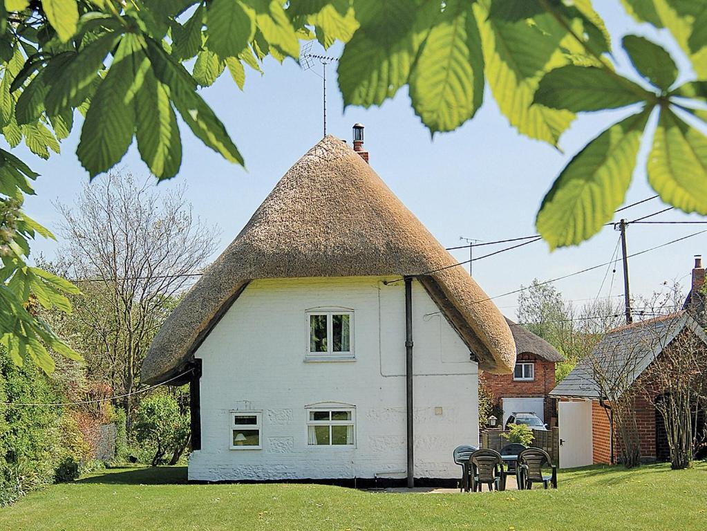 a house with a thatched roof with chairs in front of it at October Cottage in Collingbourne Kingston