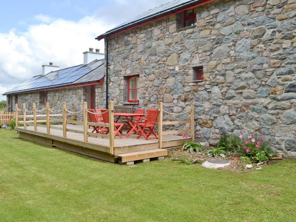 a deck with a table and chairs in front of a stone building at Ty Cai in Llanwnda