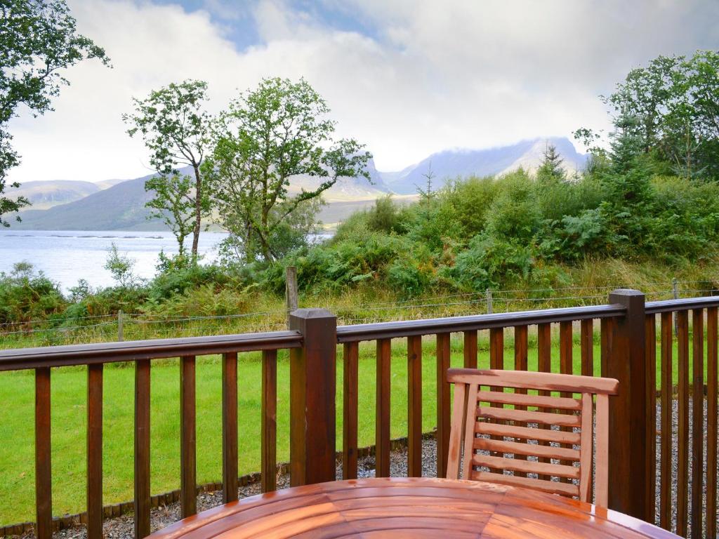 a wooden table and chair on a balcony with a view of the water at Allt Beag little Streams in Kishorn
