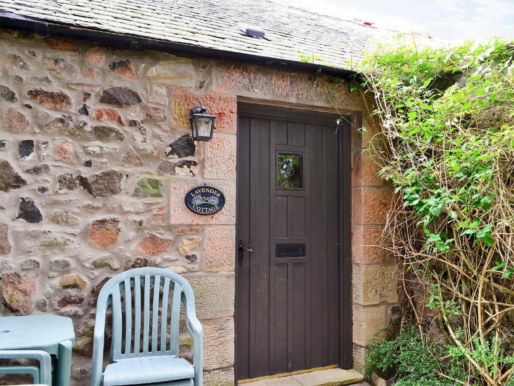 ein Steinhaus mit einer Tür und zwei Stühlen in der Unterkunft Lavender Cottage-mgg in Akeld