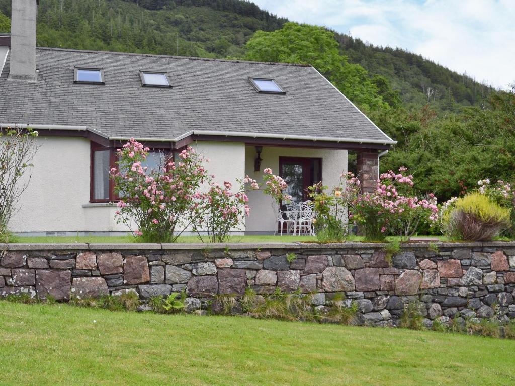 a house with a stone retaining wall and flowers at Loch Alsh Cottage - Uvo in Balmacara