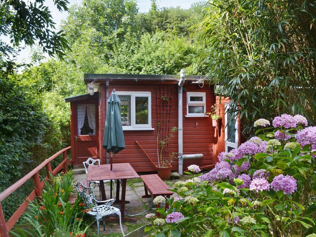 a small red house with a picnic table and some flowers at Trewartha-by-chy in Crackington Haven