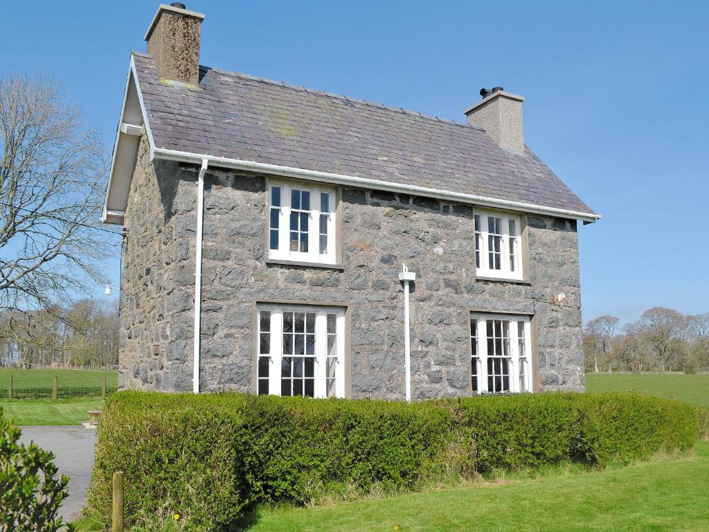 an old stone house with a hedge in front of it at Isfryn in Llanystumdwy