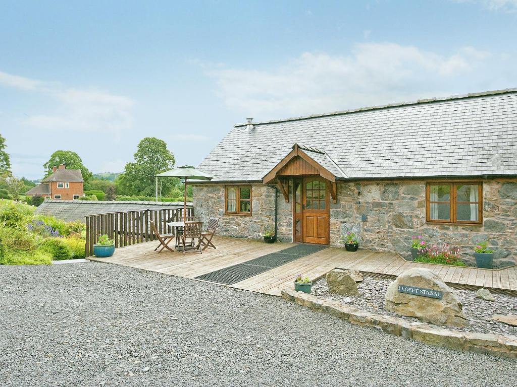 a stone cottage with a wooden deck and a table at Llofft Stabal in Llanerfyl
