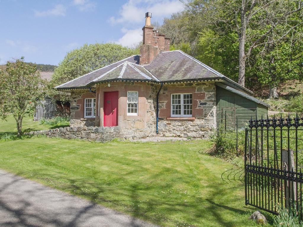een oud stenen huis met een rode deur in een tuin bij Katys Cottage in Balnaboth