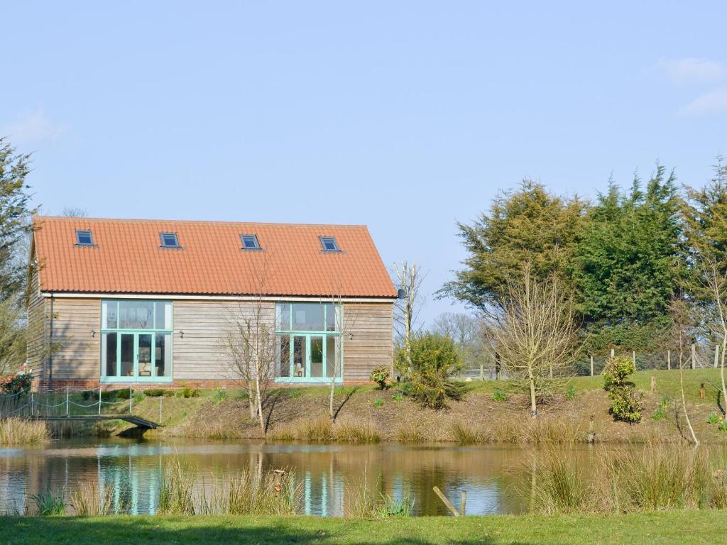 een huis met een oranje dak naast een meer bij Orchid Lodge in Hainford
