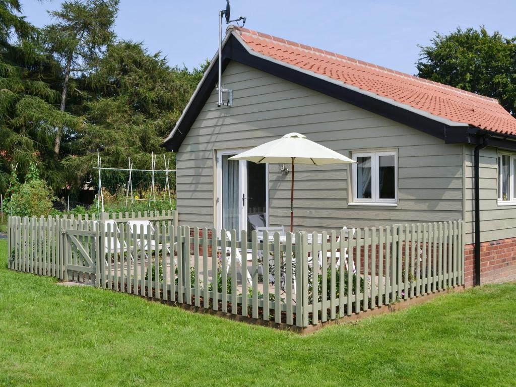 una pequeña casa con una valla blanca y una sombrilla en The Boat House, en Roughton