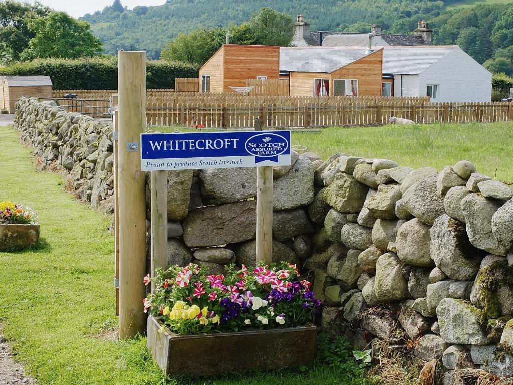 a sign in front of a stone wall with flowers at Rose Cottage - 28176 in Fairgirth