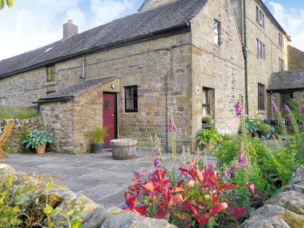 un antiguo edificio de piedra con una puerta roja y flores en Garden Cottage, en Onecote