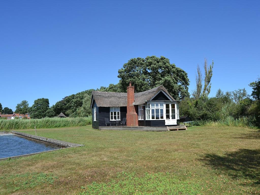 a small house on a lawn with a pond at The Studio in Hickling