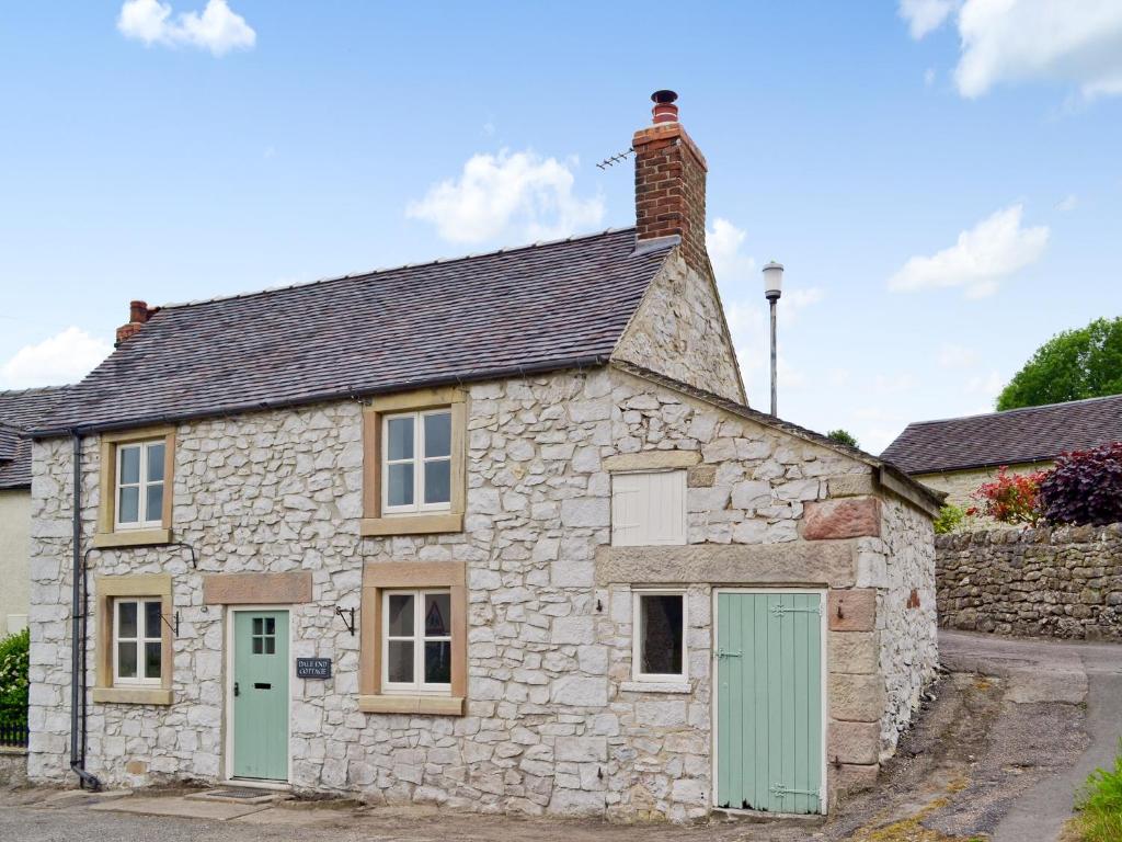 an old stone cottage with green doors on a street at Dale End Cottage in Brassington