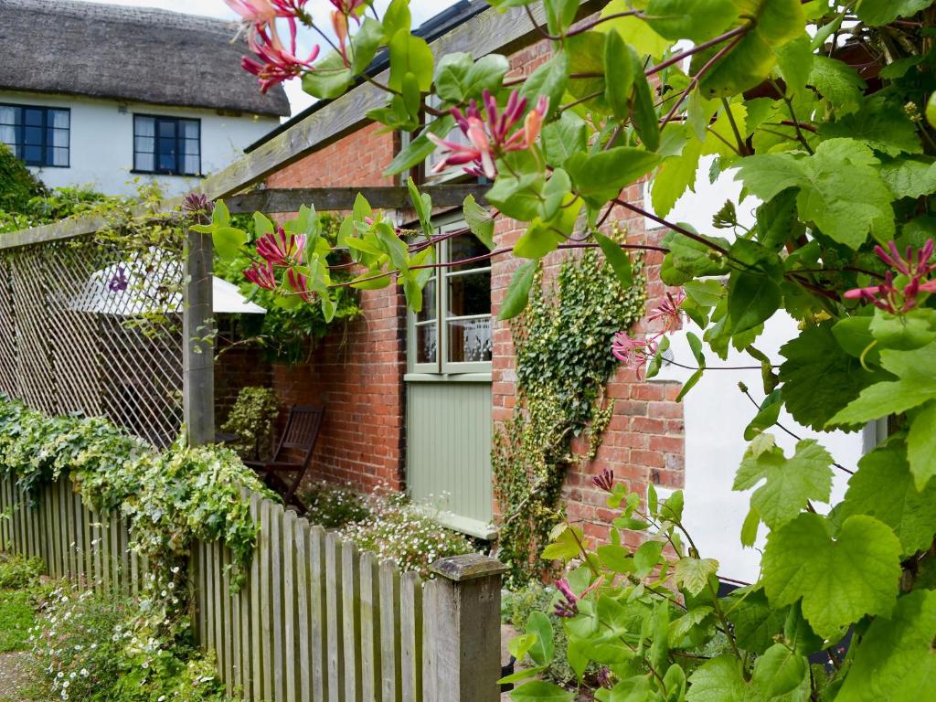 una casa de ladrillo con una valla y flores rosas en Om Shanti - 28602, en Tipton Saint John