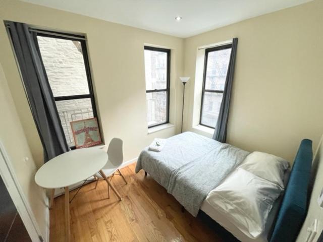 a bedroom with a bed and a desk and two windows at Budget Single Room Near Central Park in New York