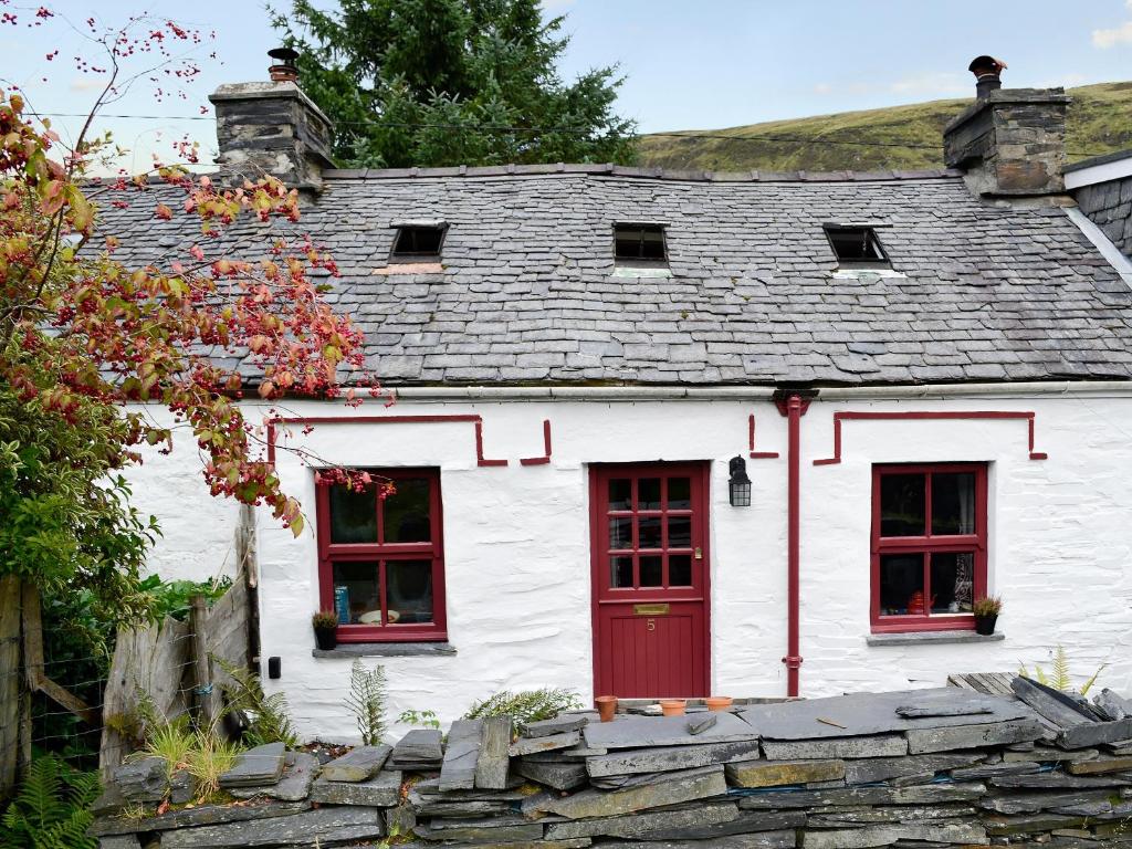 Casa blanca con ventanas rojas y pared de piedra. en Bryn Rhos Goch, en Dolwyddelan