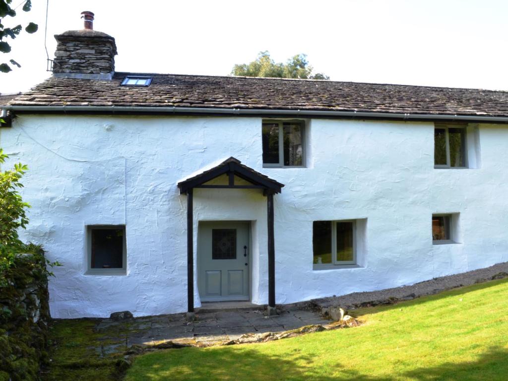 a white house with a dog sitting in front of it at Scot Beck Cottage in Troutbeck