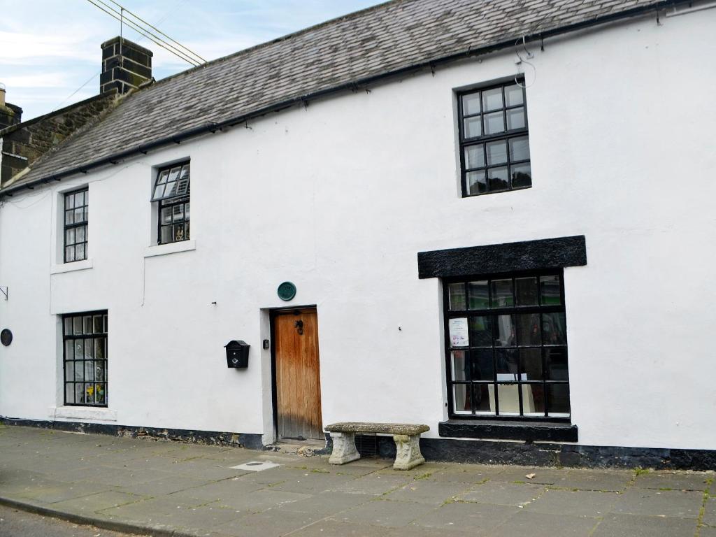 un edificio blanco con un banco delante en Grooms Bothy, en Bellingham