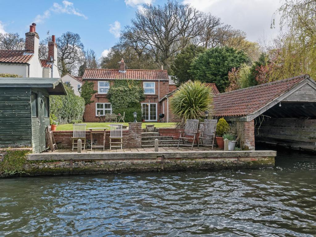 a house with chairs on a dock next to a river at Wherrymans Cottage in Coltishall