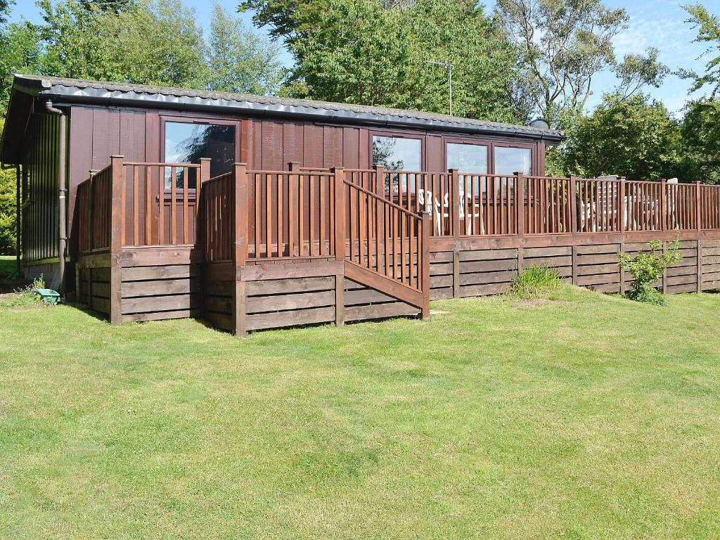 a small cabin with a wooden fence in the grass at Cedar Lodge in Palnackie