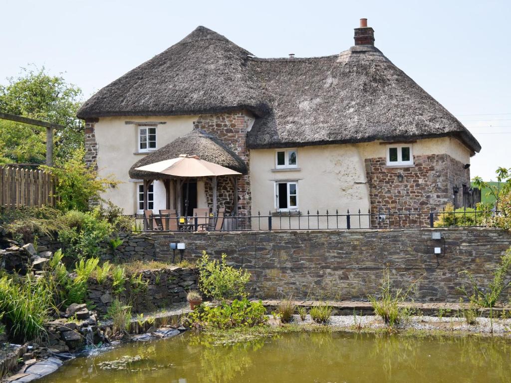 an old house with a thatched roof next to a pond at Syncocks Farm in Petrockstow