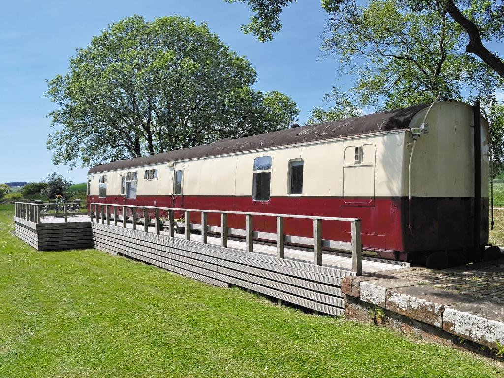 un tren rojo y blanco sentado junto a una valla en The Carriage, en Bridge of Dee