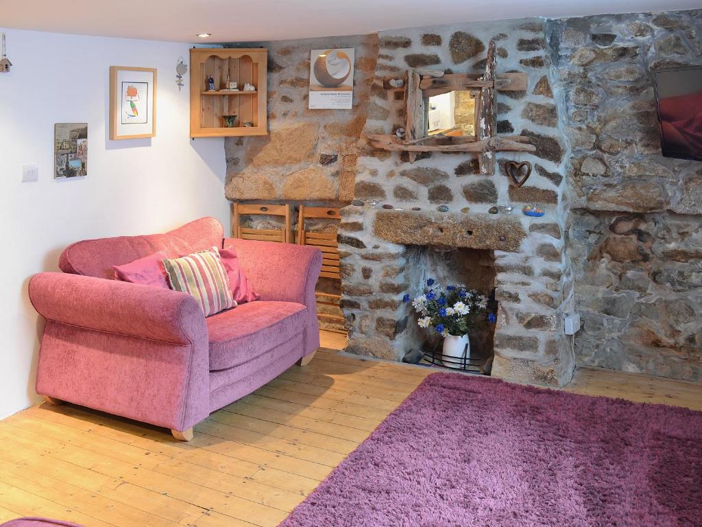 a living room with a pink chair and a stone fireplace at Driftwood in St Ives