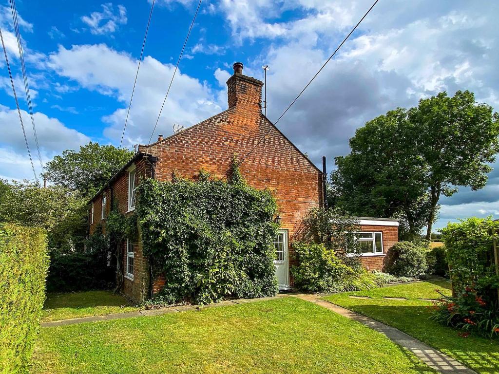 a brick house with a green yard in front of it at April Cottage in Frostenden