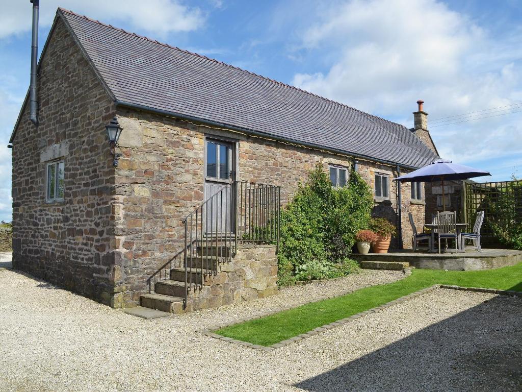 a brick house with a table and an umbrella at The Old Byre in Upper Hulme