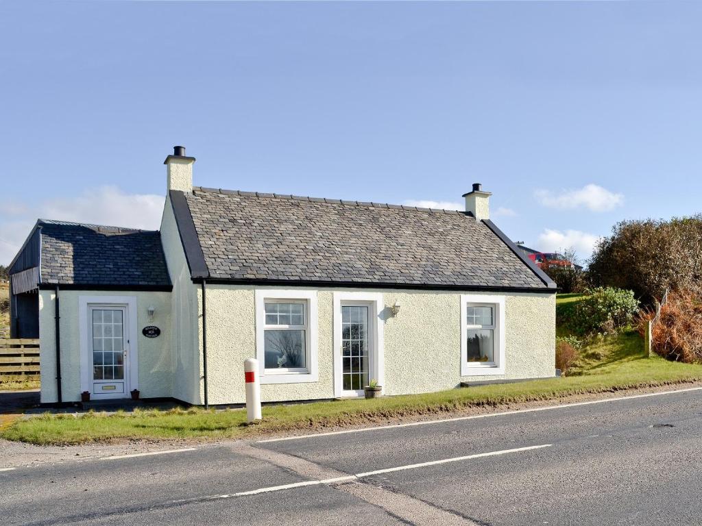 una pequeña casa blanca al lado de la carretera en Belloch Cottage, en Glenbarr