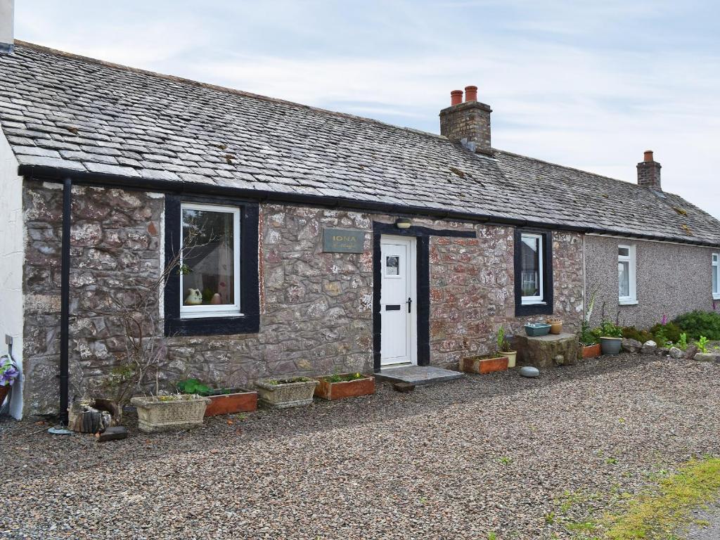 a stone cottage with a white door and windows at Iona Cottage in Clarencefield