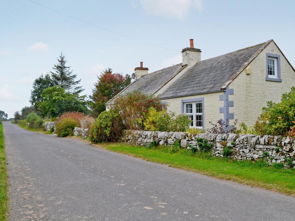 a house with a stone wall next to a road at Horsepark Cottage in Girthon