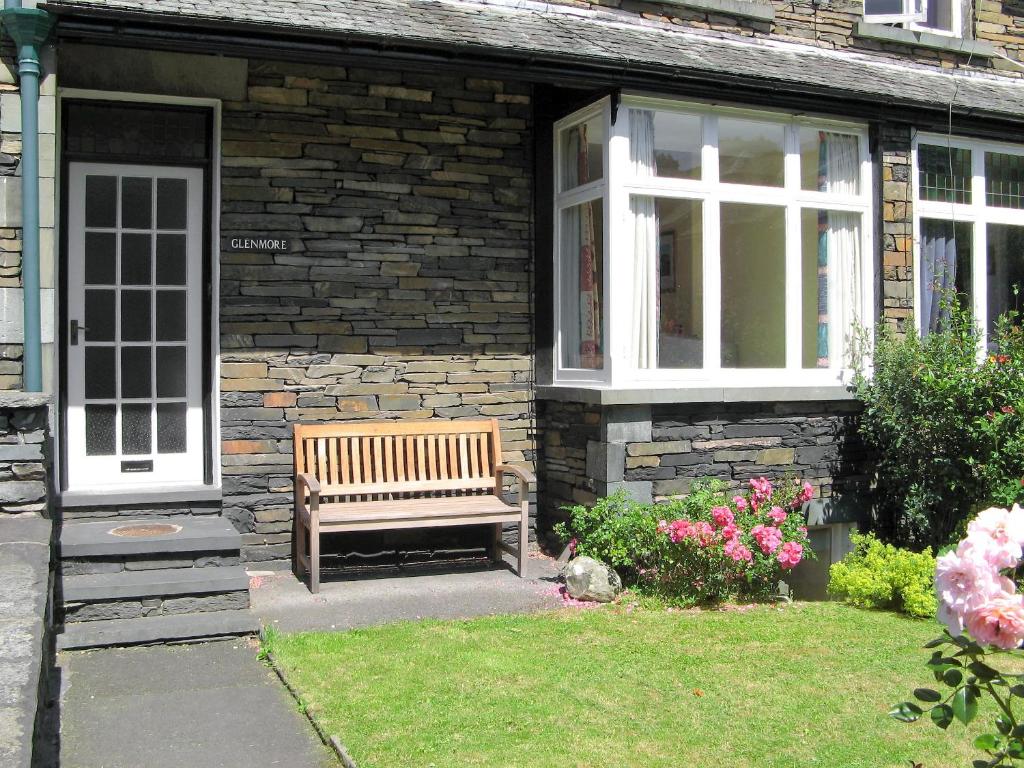 un banco de madera sentado fuera de una casa con flores en Glenmore Cottage, en Ambleside
