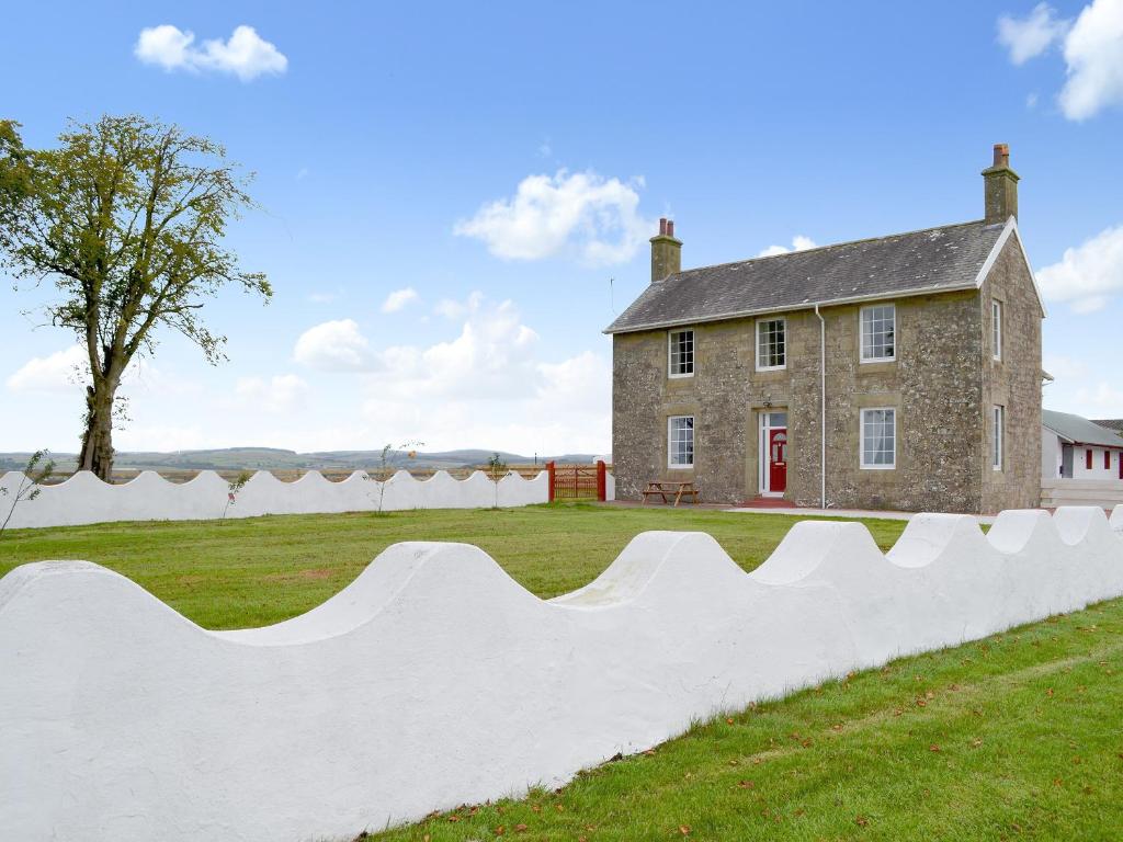 a stone house with a white fence in front of it at Bonshawside Farmhouse in Kirtlebridge